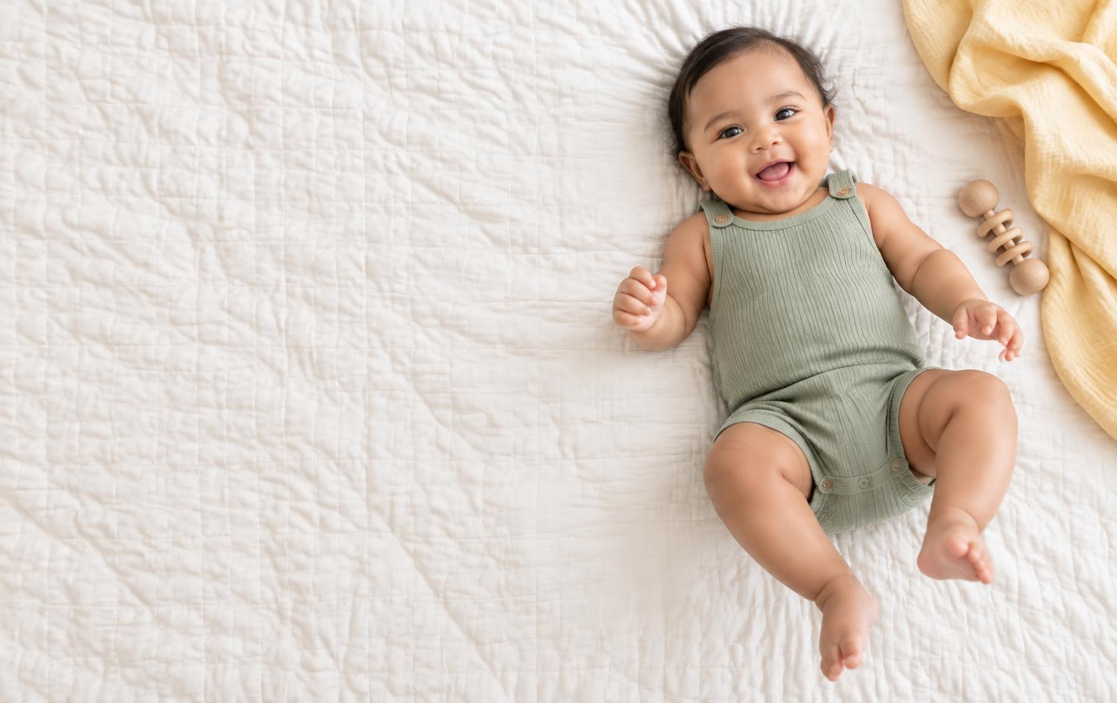 A smiling baby in a sage romper on a cotton quilt